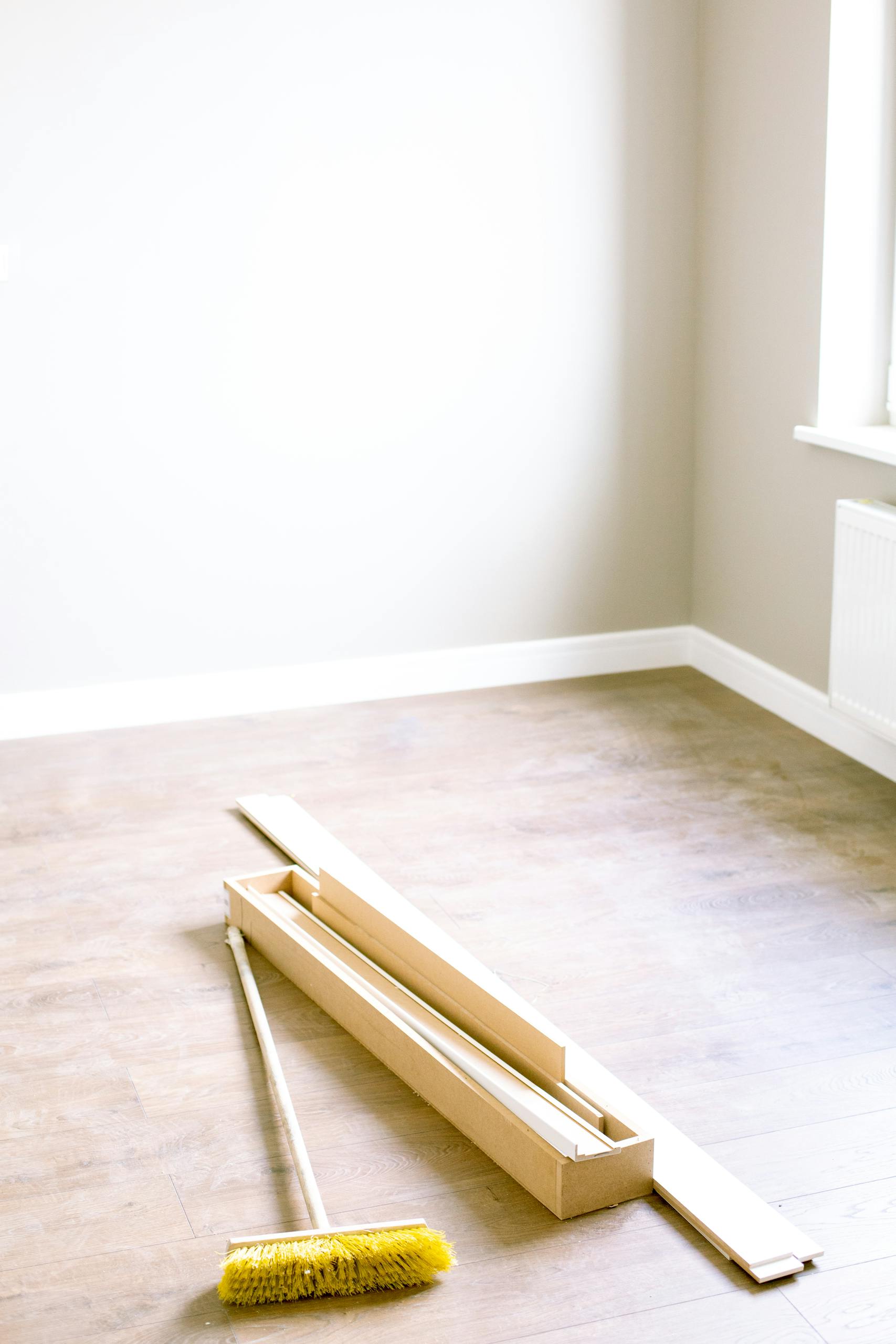 An empty room with wood planks and a broom, ready for renovation.